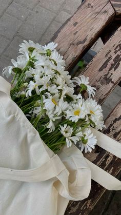 a bouquet of white daisies sitting on top of a wooden bench next to a bag