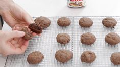 a person holding a cookie in front of some cookies on a cooling rack next to a can of nutella