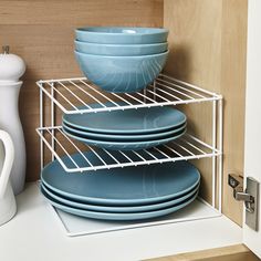 three plates stacked on top of each other in front of a shelf with two cups and saucers