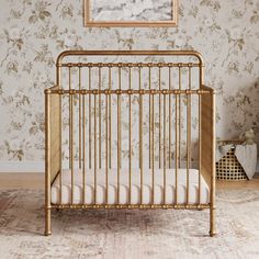 a gold crib in front of a floral wallpaper with a painting on the wall