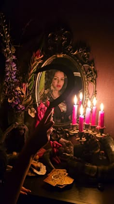 a woman looking at her reflection in a mirror with candles on the table next to it