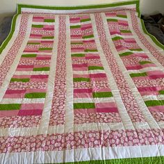 a large pink and green quilt on top of a bed with white walls in the background