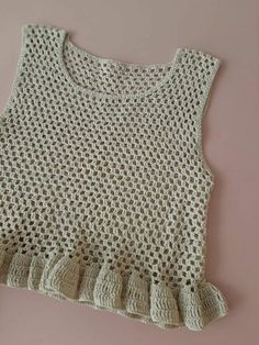 a crocheted top with ruffles on the front and bottom, against a pink background