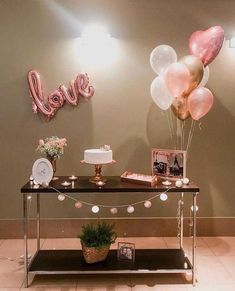 a table with balloons and cake on it in front of a wall that says love