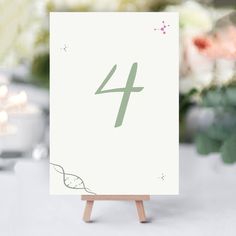 a white table number sitting on top of a wooden easel with candles in the background