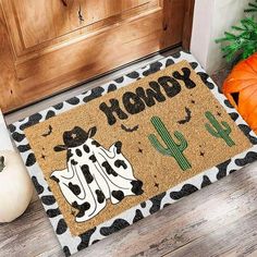 a door mat that says happy halloween with a cow and cactus on it next to pumpkins