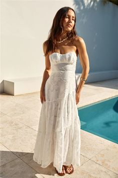 a woman standing in front of a pool wearing a white dress