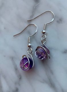 the earrings are made out of glass and silver plated wire, with purple beads hanging from them