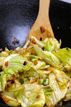 a wok filled with cooked lettuce next to a wooden spoon