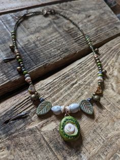 a necklace with green and white beads on a wooden table next to a piece of wood