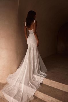 a woman in a white wedding dress standing on steps looking off into the distance with her back to the camera