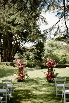 two white chairs sitting on top of a grass covered field next to trees and flowers