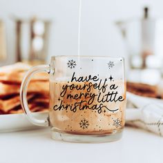 a glass mug filled with hot chocolate sitting on top of a white table next to crackers