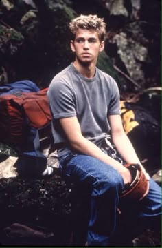 a man sitting on top of a rock next to a pile of luggage and backpacks