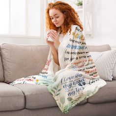 a woman sitting on a couch with a blanket over her and holding a coffee cup