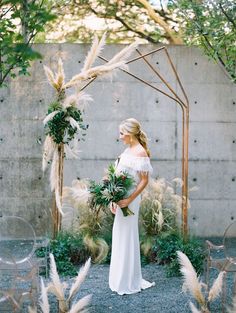 a woman in a white dress standing under an arch with flowers and greenery on it