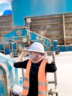 a woman in an orange safety vest and hard hat standing next to a dumpster