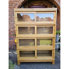 a large wooden bookcase with glass doors on the front and back sides, in front of a brick wall