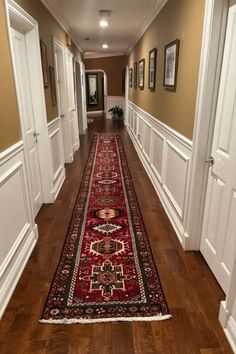 a long hallway with wooden floors and white trim on the walls is lined with framed pictures