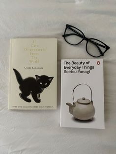 a book and glasses on a bed next to a teapot with a black cat