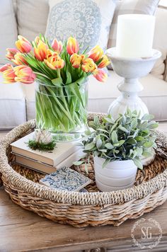 a wicker tray with flowers and books on it in front of a white couch