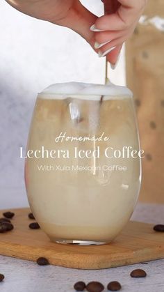 a person pouring coffee into a glass on top of a wooden board with coffee beans