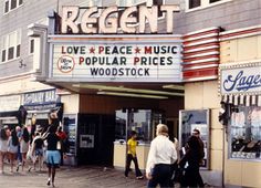 people are walking around in front of a movie theater with the marquee saying love peace music popular prices woodstock