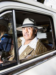 a man wearing a hat sitting in the back seat of a car with another person behind him