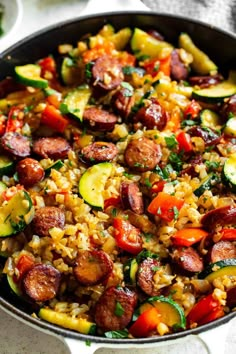 a skillet filled with sausage, rice and zucchini on top of a table