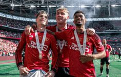 three men standing next to each other in front of a soccer stadium holding up medals