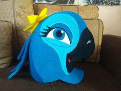 a blue bird with a yellow bow on its head sitting on a couch next to a pillow