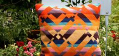 an orange and blue pillow sitting on top of a chair in front of some flowers