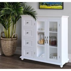 a white cabinet with glass doors next to a potted plant and wall hangings