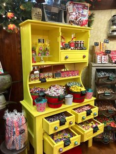 a yellow dresser with lots of candy on it's shelves and drawers in front of a christmas tree