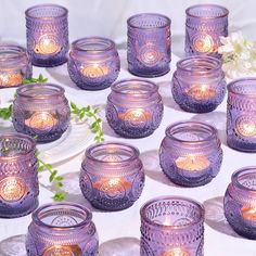 there are many purple glass candles on the table