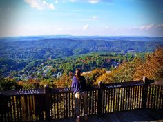 a woman standing on top of a wooden deck next to a lush green hillside covered in trees