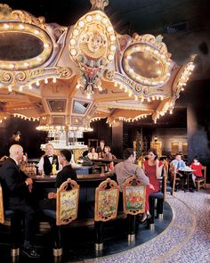 people sitting at tables in front of a carousel ride with lights on it's sides