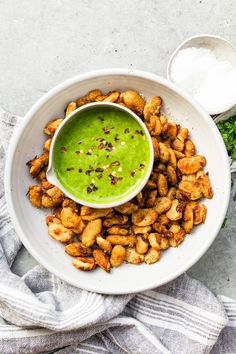 a white bowl filled with green sauce and fried chicken on a plate next to some parsley