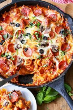 a pizza with pepperoni, olives and cheese in a skillet on a wooden table