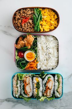 three bento boxes filled with different types of food on top of a white table