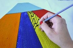 a person is holding a pencil and painting an umbrella with colorful paint on it's surface