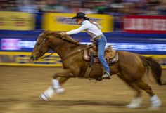 a man riding on the back of a brown horse in an arena at a rodeo