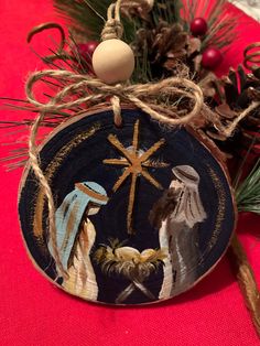 a christmas ornament with nativity scene on it and pine cones in the background