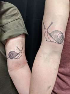 two people with matching tattoos on their arms holding each other's hands, one has a snail and the other has a shell