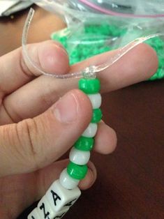 a person is holding some type of green and white beaded bracelet with letters on it