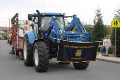 a blue tractor driving down a street next to a sign with people standing on it