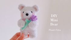 a crocheted teddy bear holding a flower in it's hand with the words diy mini bear above it