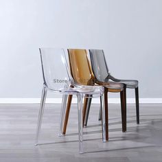 three clear chairs sitting on top of a hard wood floor next to a white wall