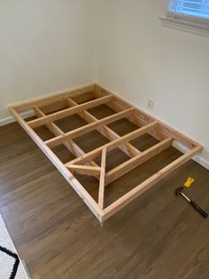 an unfinished bed frame sitting on top of a hard wood floor next to a window