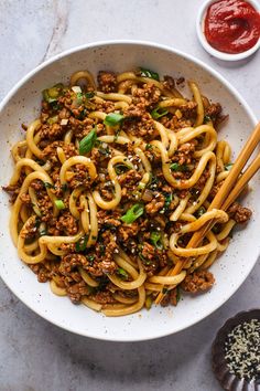 a white bowl filled with noodles and meat on top of a table next to some chopsticks